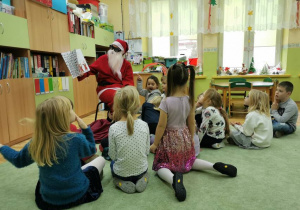Dzieci siedzą w koło czytającego Mikołaja